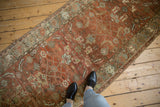 View down the length of a distressed Heriz runner's warm terracotta and green design.