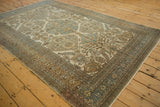 Angled view of a vintage Ardebil carpet's low, worn pile and intricate sand and blue geometric border.