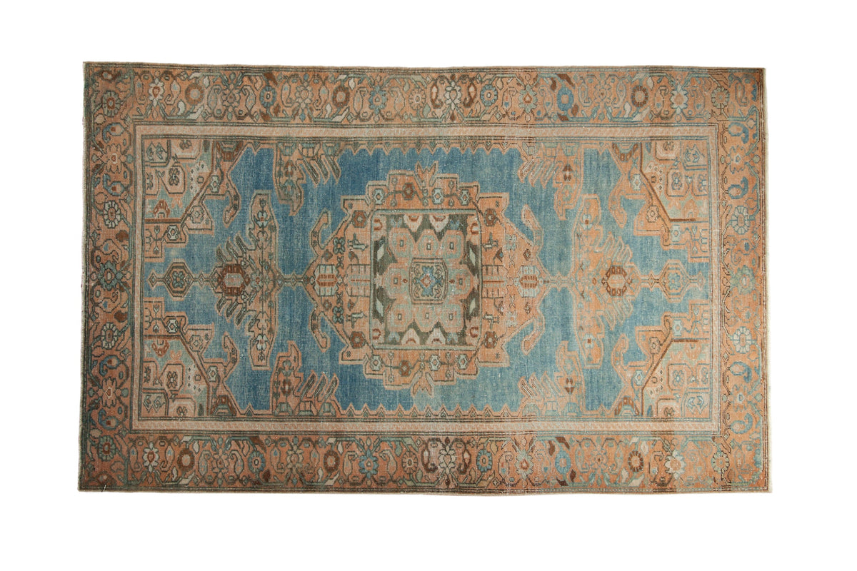 Distressed Hamadan rug with a large geometric medallion in peach and bronze on a faded blue field.
