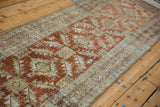 Angled view of a distressed Heriz runner showing its repeating rust and blue geometric pattern.