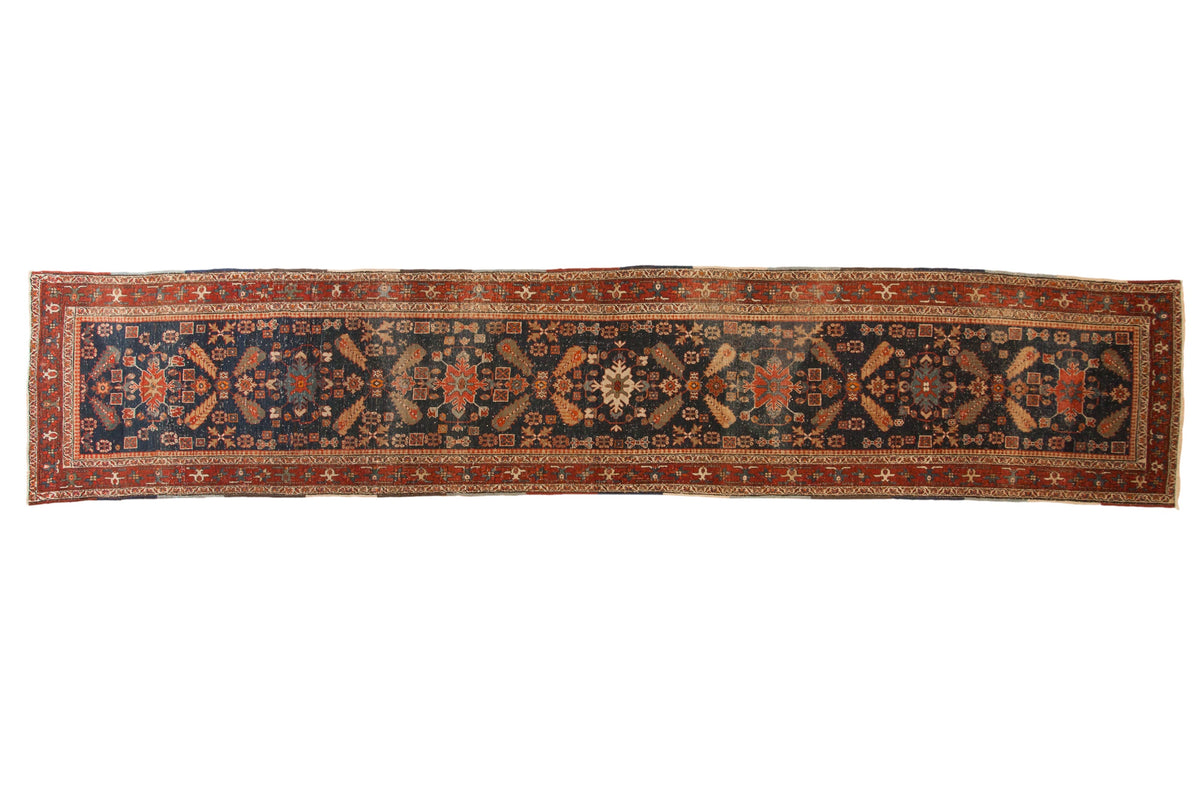 Antique Heriz rug runner with geometric cypress tree motifs on a navy blue field and brick red border.