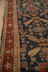Angled view of an antique Heriz runner's geometric red border and navy field with time-softened pile.