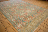 An angled view of a vintage Caucasian carpet showing its geometric palmette border and worn pile.