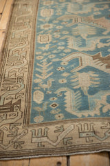 Angled view of a distressed Malayer rug's geometric border against a sky blue field with stylized birds.
