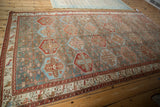 Vintage Baktiari carpet shown at an angle, featuring its distressed hexagonal panel design in slate blue and red.