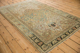 Angled view of a vintage Sarouk rug showing the dusty teal shield medallion and floral vine field.
