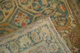 A folded corner of the distressed Sarouk rug reveals its hand-knotted back and low pile texture.