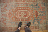 A person's-eye view of a distressed Bijar rug's soft, faded red and powder blue pattern.