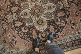 Close view of a distressed Hamadan rug's starburst medallion in dusty rose and charcoal brown.