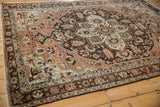 Angled view of a distressed Hamadan carpet with its charcoal medallion and copper rose palmettes.