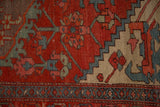 Antique rug's geometric vine border and low-pile texture in brick red and faded blue hues.
