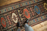 A person's perspective looking down a vintage Kurdish runner with octagonal guls and tribal figures.
