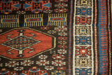 A red octagonal gul and multi-colored geometric border on the dark brown hand-knotted pile of a Kurdish rug.