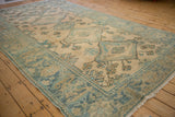Angled view of a distressed Malayer carpet, highlighting its wide floral border and low-pile texture.