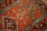 Angled detail of a stepped medallion with arrowed coloration on a brick red Persian rug.