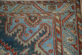 Corner detail of a vintage Malayer carpet with serrated geometric motifs in blue and red.