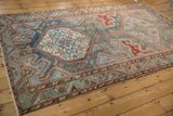 Angled view of a distressed vintage Malayer carpet, showing its geometric medallions and faded colors.