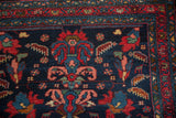 Mehreban rug detail: navy field featuring red palmettes, serrated creatures, and vine border.