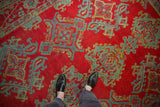 The low, hand-knotted pile of a vintage Oushak carpet in cherry red with sky blue and gold geometric details.