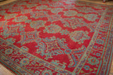 Low angle view showing the even wear and texture of a vintage Oushak carpet's red, blue, and gold pattern.