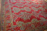 Angled view of a red Oushak carpet, focusing on the sky blue floral bouquets within the border.