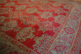 Texture of the antique Oushak's low pile, showing the slate blue meandering vine border and red field.