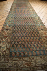 A long perspective of a distressed Persian runner showing rows of botehs on a sapphire blue field.