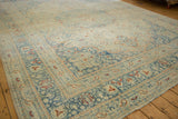 A low angle view across a vintage distressed carpet showing its sprawling pattern in dusty blue and cream.