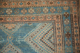Corner detail of a distressed Malayer rug with geometric borders and checkered patterns in sky blue and coffee brown.