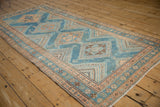 Angled view of a distressed Malayer runner, showing the repeating diamond medallions down its length.