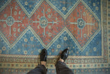 Close-up of the distressed pile and geometric pomegranate medallion on a vintage Caucasian rug in rose and blue.