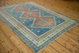 Angled view of the distressed vintage Caucasian rug, showing its abrashed blue field and ruby red medallions.