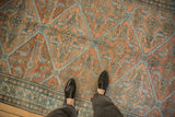A close perspective of the distressed, low pile of an antique Malayer carpet in terracotta and dusty blue tones.