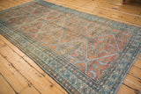 A distressed antique Malayer carpet from an angle, showing its geometric lattice in terracotta and blue.