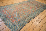 Angled view of a distressed Malayer carpet's terracotta diamond lattice and detailed blue boteh border.