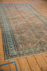 Angled view of a distressed Malayer carpet showing its full length and terracotta and blue lattice design.