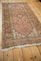 Angled view of a distressed Heriz rug showing its geometric pattern in dusty blush and faded silver.