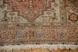 Corner of a distressed Heriz rug showing the geometric border, worn pile, and ivory fringe.