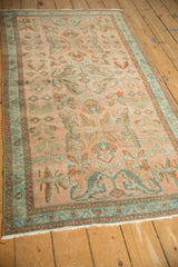 Lengthwise view of a distressed Persian rug with a dusty blush field and teal borders.