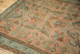 Corner view of a vintage Lilihan rug showing the worn pile, teal border, and floral patterns.