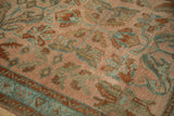 Close-up on the distressed rug's low pile, showing the texture of dusty teal and rust floral arabesques.