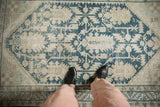 Looking down at the distressed texture of a vintage Hamadan rug with dusty blue floral motifs.