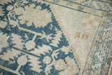 Corner detail of a distressed Persian rug showing its low pile and a serrated blue palmette.