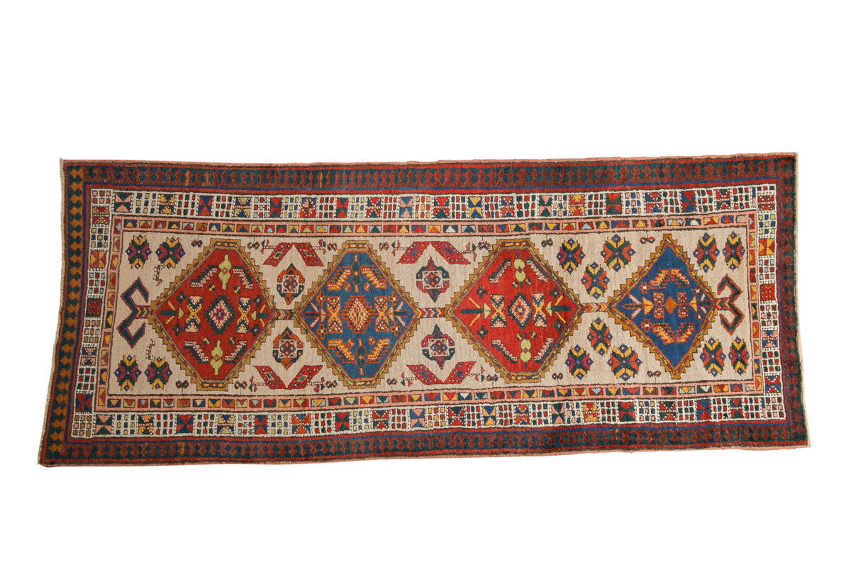 Vintage Serab rug runner with repeating diamond medallions in sapphire blue and ruby red on a sand field.