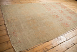 Angled perspective on a vintage Oushak carpet showcasing its heavy abrashes and muted blush geometric motifs.