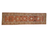 Antique distressed Caucasian runner with a geometric floral lattice in rust, ochre, and charcoal tones.