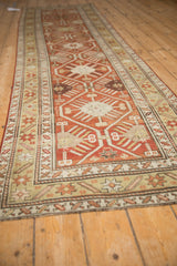 Angled view of the antique Caucasian runner's geometric lattice design in rust, gold, and charcoal.
