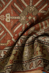 Close-up on a folded antique Caucasian rug showing its low pile and geometric starburst motifs.