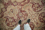 Detailed texture of a vintage Kerman rug with worn burgundy and teal motifs over an ivory field.