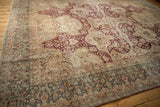 Angled view of a distressed vintage Kerman carpet showing its scale, burgundy motifs, and teal border.